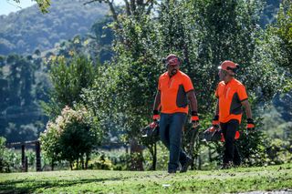 Dos personas caminando sobre la hierba, cargando productos Husqvarna en un jardín.