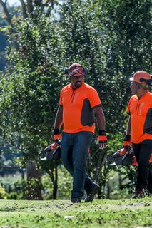 Dos personas caminando sobre la hierba, cargando productos Husqvarna en un jardín.