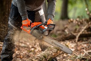 A person using a Husqvarna chainsaw to cut a tree branch in a forest setting.
