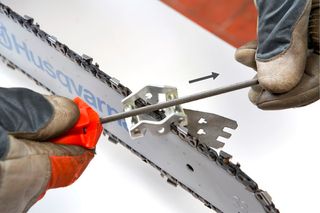 Close-up of a person adjusting a chainsaw chain with a tool.