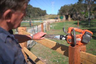 A person holding a chainsaw on a wooden fence in a rural setting.