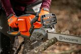 A person using a Husqvarna chainsaw to cut a tree branch outdoors.