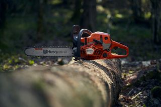 Una motosega Husqvarna appoggiata su un tronco d'albero caduto in un ambiente forestale.