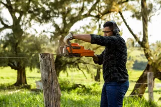 A person using a chainsaw to cut a tree stump in a grassy outdoor setting.