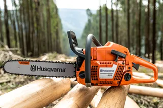 Ланцюгова пилка Husqvarna спирається на спиляні колоди дерев у лісі.