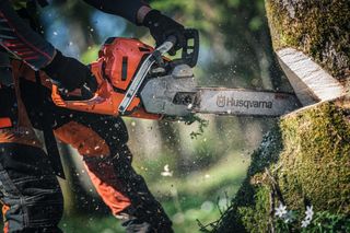 A person using a Husqvarna chainsaw to cut a tree trunk outdoors.