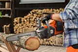 A person using a chainsaw to cut a log outdoors, with stacked logs in the background.