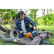 Une personne utilisant une scie à chaîne pour couper des branches d’arbres dans un jardin.