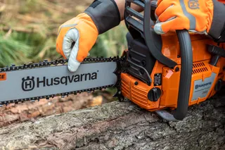 A person wearing work gloves using a Husqvarna chainsaw to cut a log.