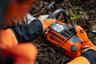 A person using a Husqvarna chainsaw to cut a tree trunk in a forest setting.