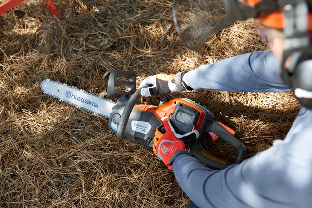 Una persona che utilizza una motosega Husqvarna su un letto di aghi di pino.