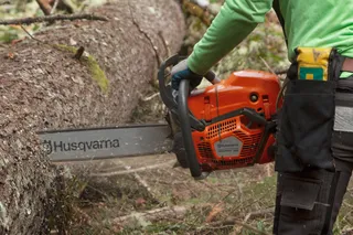 Людина використовує ланцюгову пилку Husqvarna для розрізання поваленого дерева в лісі.