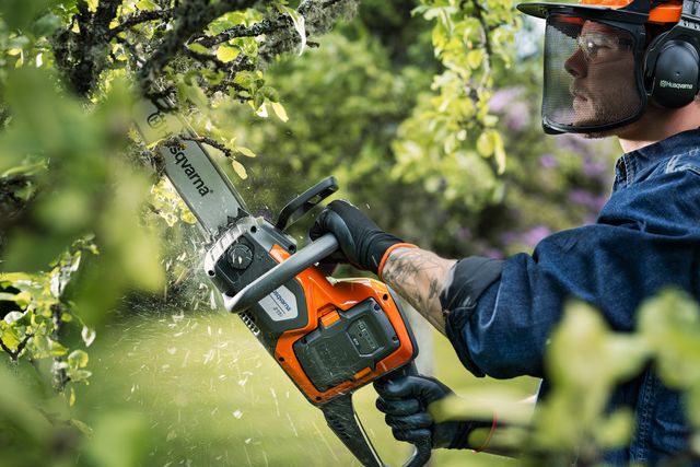 A person using a chainsaw to trim tree branches in a garden.