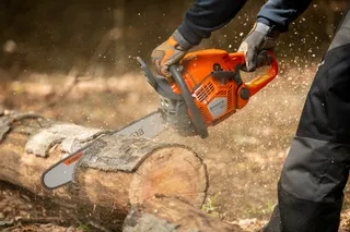 A person using a chainsaw to cut a log outdoors.