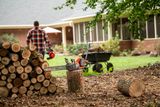 A person walking away from a stack of cut tree logs, with a chainsaw and helmet placed on a log.