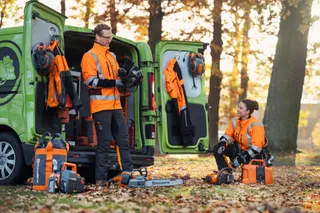 Två arbetare i en skogsmiljö med motorsåg och tillbehör från Husqvarna, nära en skåpbil.