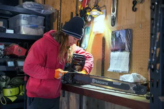 A person in a workshop setting adjusting a Husqvarna chainsaw on a workbench.