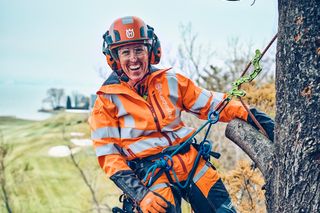 Arborister i arbetskläder som klättrar i ett träd med en motorsåg fäst vid selen.