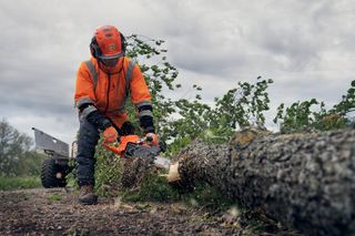 Husqvarna X-CUT® S93G, 3/8" mini pitch, .050 gauge. A person in work gear using a chainsaw to cut a fallen tree trunk outdoors.