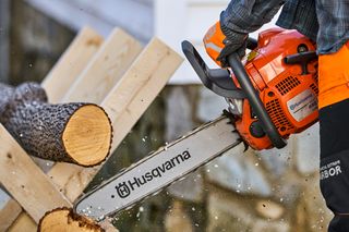 Osoba używająca piły łańcuchowej Husqvarna do cięcia drewnianych kłód na zewnątrz.