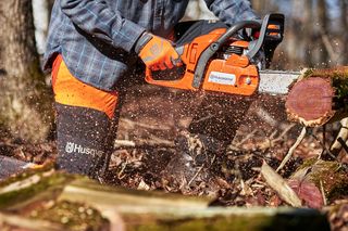 A person using a chainsaw to cut logs in a forest setting.
