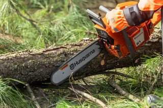 A person using a chainsaw to cut a fallen tree branch.