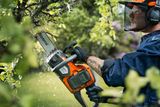 Person pruning tree branches with a chainsaw, wearing work helmet with visor and gloves.