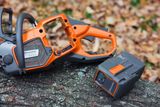 En motorsåg från Husqvarna placerad på en trädstock med ett batteri bredvid.