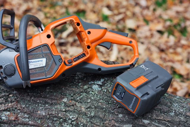 Husqvarna-moottorisaha, joka on asetettu puun puuhun ja jonka vieressä on akku.