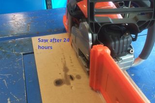 Chainsaw with a protective cover on a workbench, showing oil stains on cardboard after 24 hours.