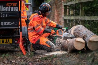 Husqvarna X-CUT® S93G, 3/8" mini pitch, .050 gauge. A worker using a chainsaw to cut tree logs next to a wood chipper on a roadside.