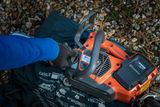 Une personne inspecte une tronçonneuse Husqvarna sur un sol couvert de cailloux et de tissu.