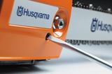 Close-up of a Husqvarna chainsaw being adjusted with a screwdriver.