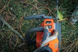 A person operating a chainsaw in a forest setting, focusing on the control panel.