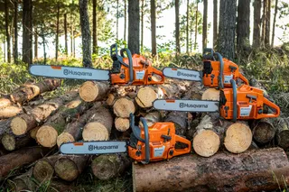 Two Husqvarna chainsaws resting on a stack of cut tree logs in a forest setting.