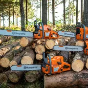 Two Husqvarna chainsaws resting on a stack of cut tree logs in a forest setting.