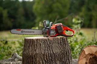 A Husqvarna chainsaw resting on a tree stump in a forest setting.