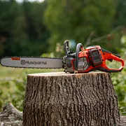 A Husqvarna chainsaw resting on a tree stump in a forest setting.