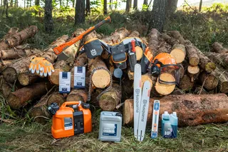 A collection of Husqvarna chainsaw accessories including a chain, oil, and protective gloves, set against a backdrop of stacked tree logs in a forest setting.