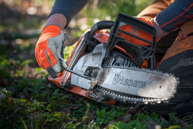 A person adjusting the chain tension on a Husqvarna chainsaw in a grassy area.