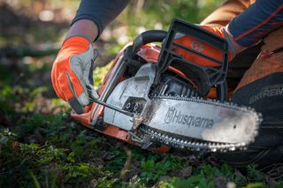 Una persona che regola la tensione della catena su una motosega Husqvarna in un'area erbosa.