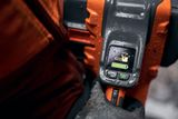Närbild av en handskbeklädd hand som håller ett verktyg med en digital display som visar batterinivåer och en motorsågsikon.