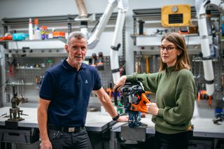 Two people in a workshop setting, with one person holding a chainsaw on a workbench.