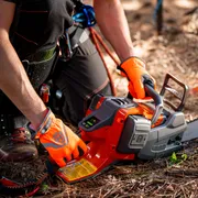 A person kneeling on the ground, inspecting a Husqvarna chainsaw in a forest setting.
