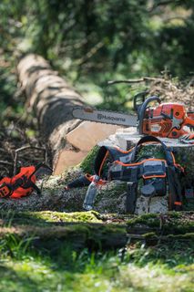 Una motosega Husqvarna e i relativi accessori collocati su un ceppo d'albero in un ambiente forestale.