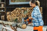 Person cutting a tree log on sawhorses with a chainsaw on a wooden deck.