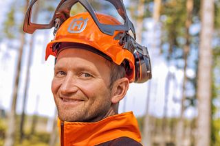 Isik, kes kannab Husqvarna kaitsekiivrit koos kõrvakaitsete ja visiiriga metsas.