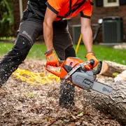 A person using a chainsaw to cut a fallen tree trunk outdoors.