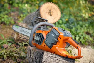 Husqvarna 435i. A Husqvarna chainsaw resting on a cut tree log in a garden setting.