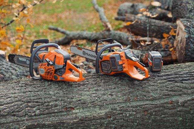 Two Husqvarna chainsaws placed on a large tree log in a forest setting.
